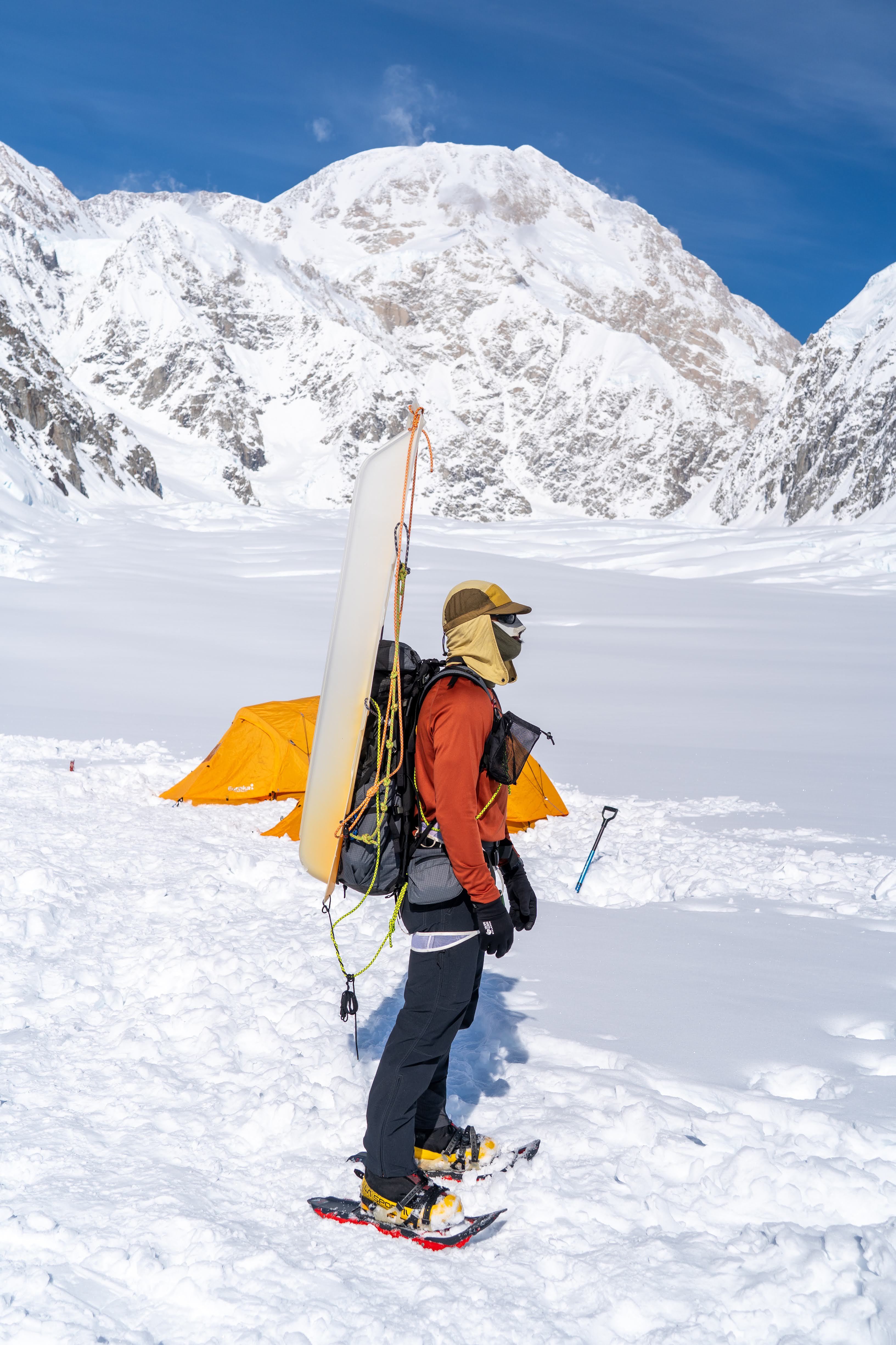 A mountaineer in full expedition gear stands at a basecamp in the snow