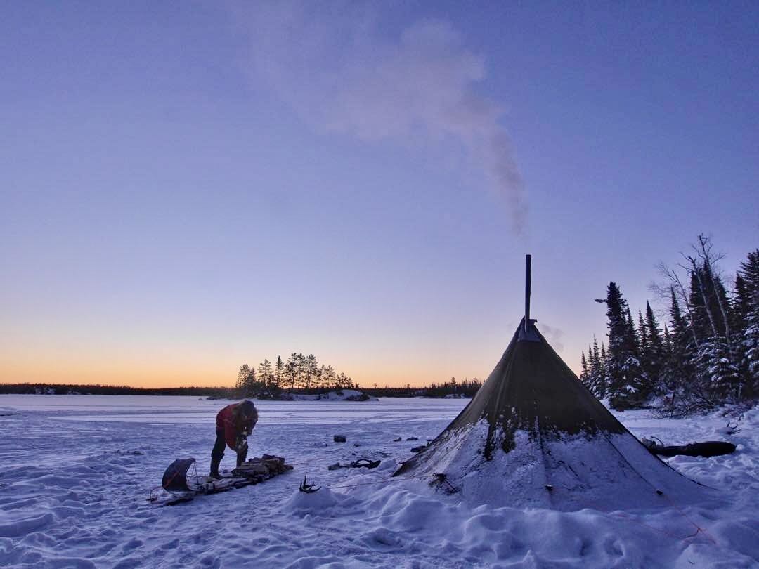 tipi pitched in deep snow, smoke curling from the chimney pipe