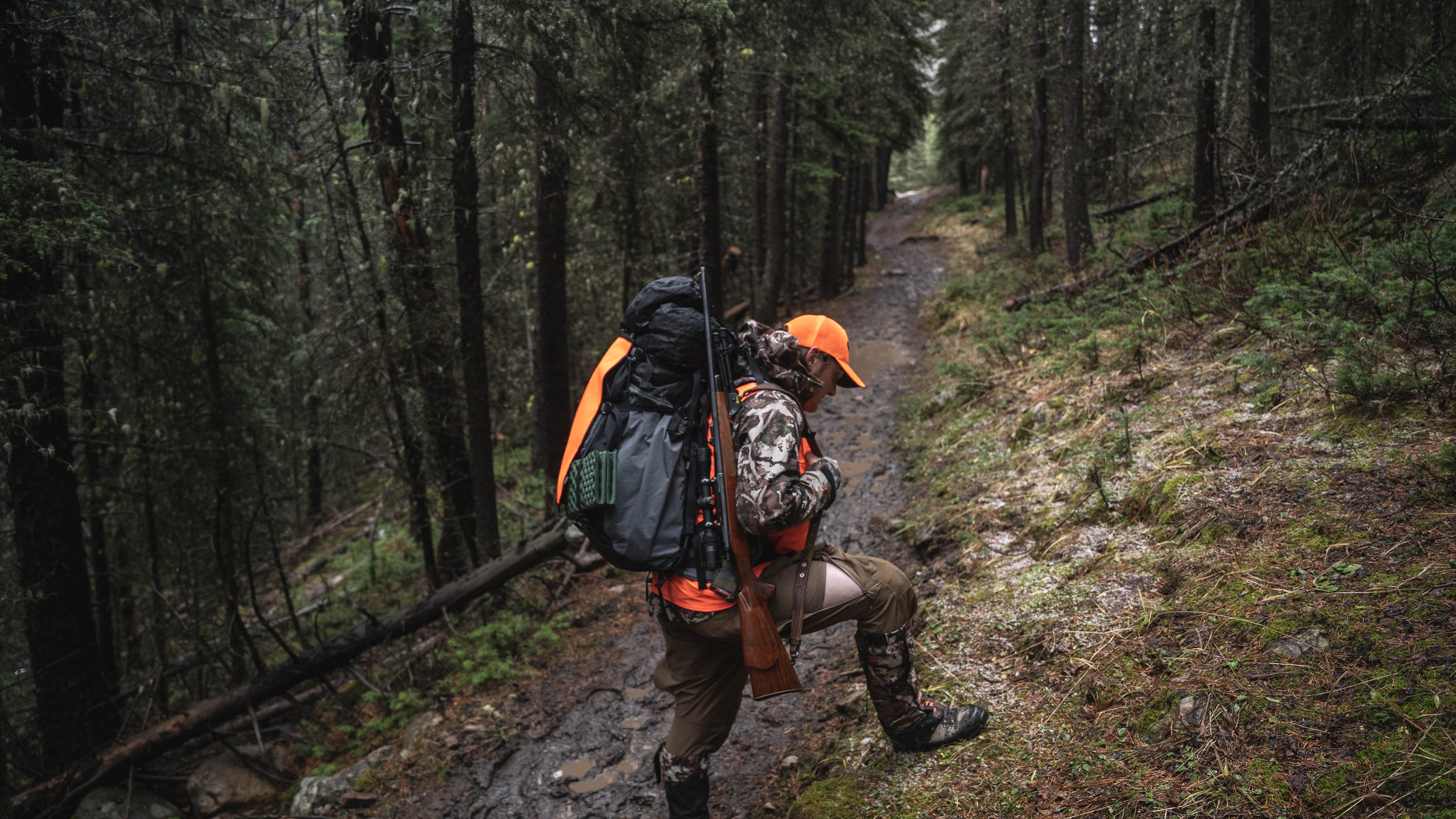 hunter with heavy pack crosses a trail on a steep mountainside